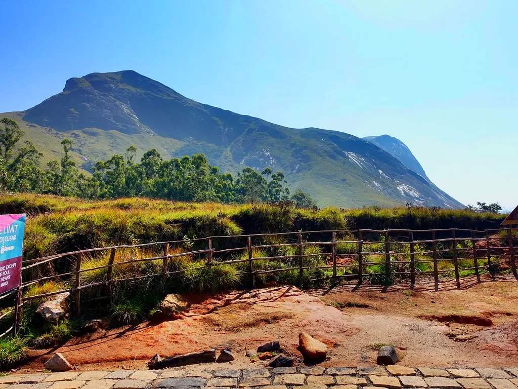 Grassland path and wooden fence below a granite summit in the Western Ghats
